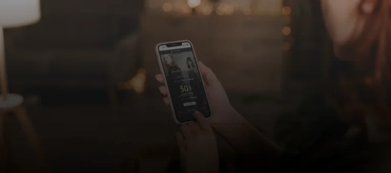 Pessoa segurando um celular, acessando o site da sacada para compras online, em ambiente interno com iluminação quente.